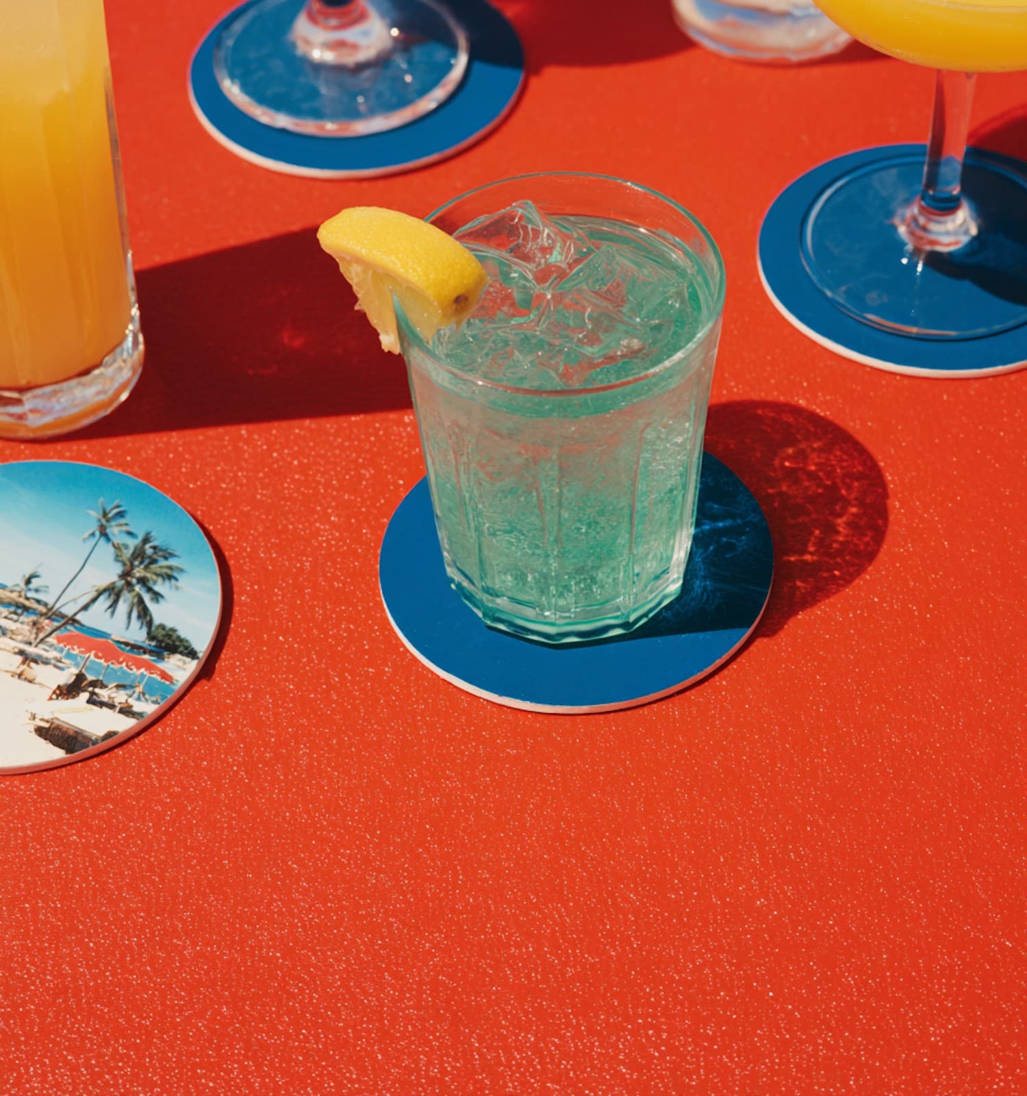 Sparkling drink with a lemon wedge on a blue coaster on a red tabletop